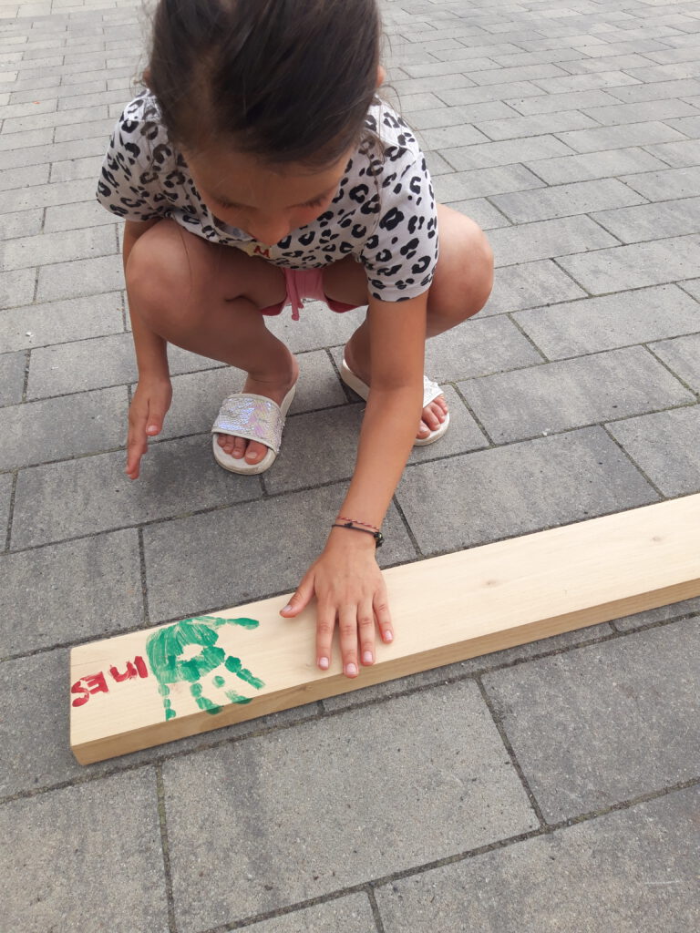 Bilder der Kinder, die mit Freude ihre Handabdrücke auf dem Holz verewigen